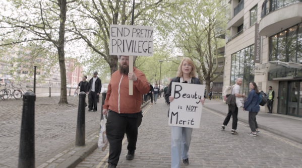Protesters marching with signs including 'END PRETTY PRIVILEGE' and 'Beauty is NOT Merit'